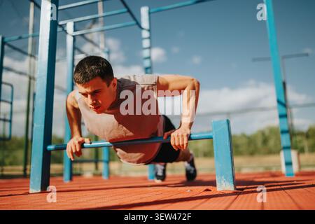 Young man doing push-ups on parallel bars at outdoor fitness park on a sunny day Stock Photo