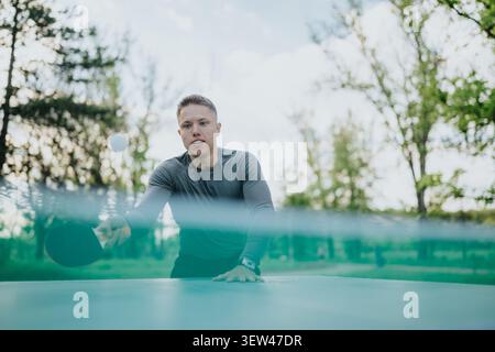 Young man playing table tennis outdoors in a park wearing an athletic long sleeve shirt Stock Photo