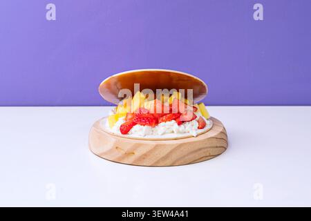 Open wafer shell filled with cream and topped with fresh strawberries and mango chunks, displayed on a round wooden base. Stock Photo