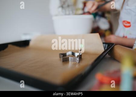 Mom and child preparing a star cookie cutter on a parchment-lined baking tray in home kitchen Stock Photo