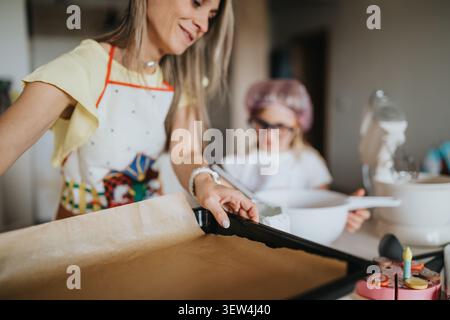 Mom and child baking together at home preparing a parchment-lined tray in a bright kitchen Stock Photo