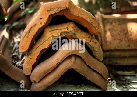 A detailed close-up showing a stack of old, weathered terracotta clay ridge roof tiles featuring chipped edges and visible cracks from age. Stock Photo