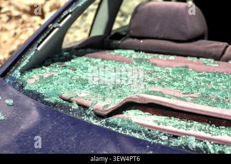 Close-up view of countless green tempered glass shards piled on the rear shelf inside a car with a shattered back window. Stock Photo