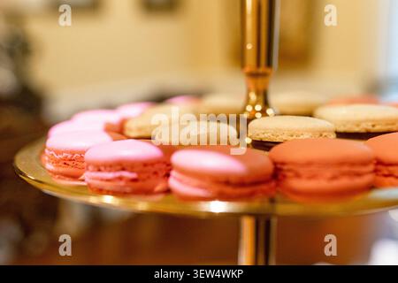 Pink and peach French macarons arranged on a gold tiered dessert stand at a baby shower, shallow depth of field, USA. Stock Photo
