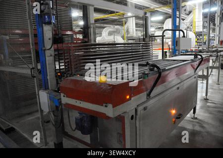 Automated conveyor system transporting ceramic tiles in a manufacturing plant. Industrial machinery processes stacked tiles on rollers in a modern cer Stock Photo