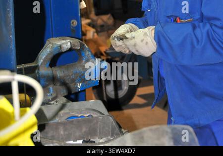 Worker wearing gloves inspects a metal part near a vise in a workshop, showing manual craftsmanship, precision work, and industrial maintenance activi Stock Photo