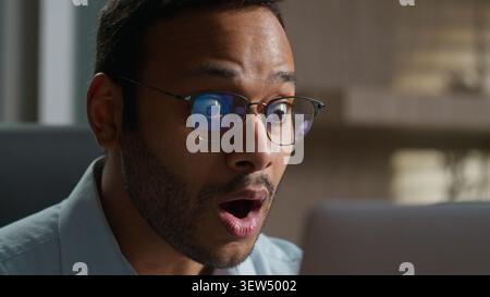 Shocked Indian Arabian business man staring laptop screen indoor office stressed confused American businessman male worker employer in glasses afraid Stock Photo