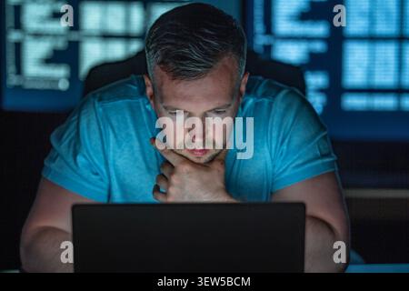 Programmer analyzes code in dark room. Programmer writes programming for secure software. Programmer monitors network and database. Programmer Stock Photo