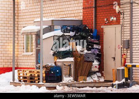 Pile of discarded plastic crates and stacked cardboard boxes piled up behind a small urban kiosk shop on a snowy winter day: Russia - January 17, 2026 Stock Photo