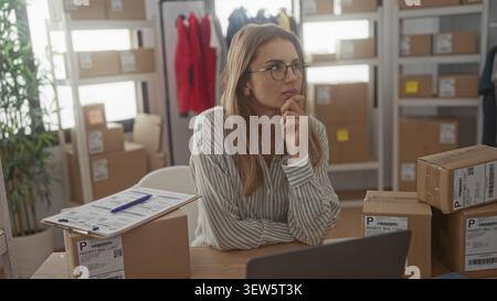 Woman packing packages and checking shipping labels, hand on chin while handling a parcel in a studio workspace; thoughtful planning. Stock Photo