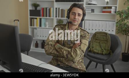 Soldier man typing with headset, hands on keyboard and dog tags visible while using a desktop computer at a desk with bookshelves and a backpack in an Stock Photo