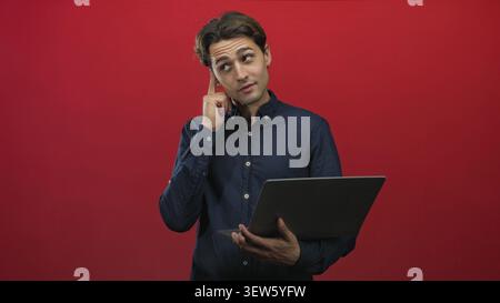 Man holding laptop with finger to chin in studio, looking up while evaluating ideas amid a red backdrop and shifting poses across frames; thoughtful f Stock Photo