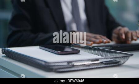 Close up male hands typing computer keyboard African American business man working online at office table with papers folders mobile phone Stock Photo