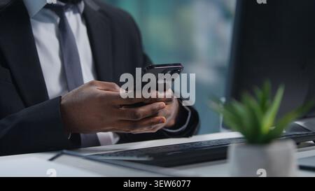 Cropped view African American business man chatting mobile phone app at office table with computer. Close up unrecognizable male businessman Stock Photo