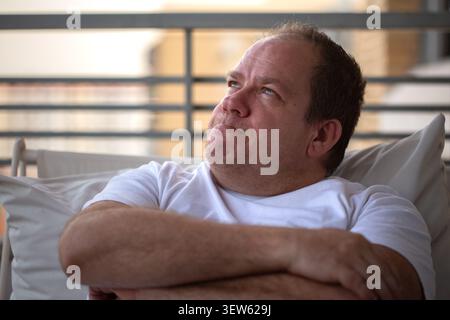 Thoughtful middle-aged man sitting on sofa looking away in contemplation Stock Photo