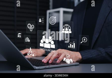 Outsourcing business concept. Businessman using laptop, virtual interface icons showing third party remote team vendor, global resource management, Stock Photo