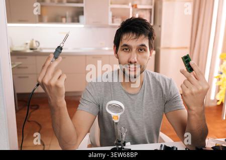 Man holding soldering iron and electronic microchip, ready for technical repair, assembly, embodying concepts of engineering, diy, technological Stock Photo