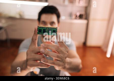 Man holding small green circuit board with microchips and memory module, close-up on hand concept of computer hardware components for inspection Stock Photo