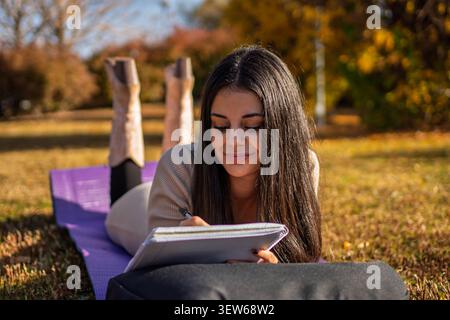Young woman writing in notebook, relaxing on a yoga mat in an autumn park Stock Photo