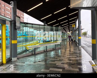 View of the Liverpool One Bus Station terminal, showing glass partitions, yellow seating, and parked double-decker buses in Liverpool, UK. Stock Photo
