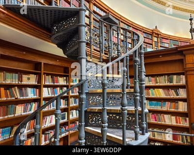 Victorian iron spiral staircase in the Picton Reading Room, Liverpool Central Library. The circular room features tiered wooden bookshelves. Stock Photo