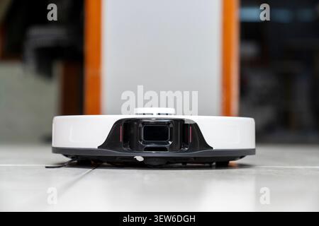 Modern robotic vacuum cleaner cleaning dust on a tile floor in a smart home. Automated housekeeping and wireless smart cleaning technology. Stock Photo