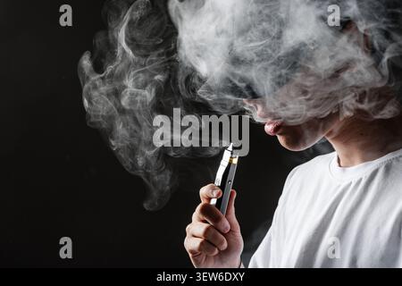 A close-up of a vaper inhaling from an electronic cigarette, surrounded by thick vapor clouds, highlighting the dangers of nicotine addiction and Stock Photo