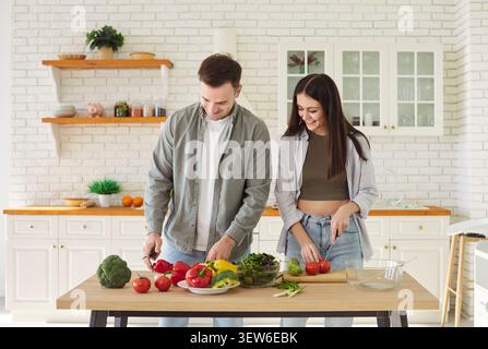 Happy young couple cooking together in kitchen, cutting fresh vegetables and preparing healthy salad Stock Photo