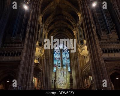 Interior of Liverpool Cathedral, Liverpool. Gothic Revival architecture featuring towering stone arches and illuminated stained glass window. Stock Photo