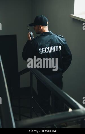 Bodyguard in uniform using walkie talkie while walking down stairs indoors Stock Photo