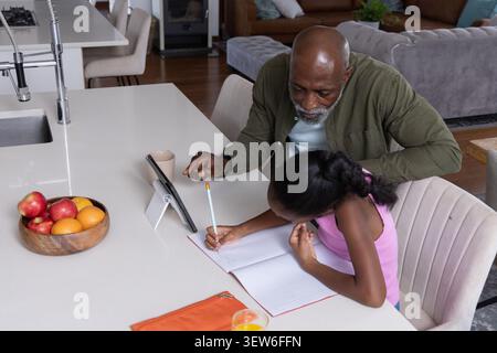 African American senior man guiding girl writing at kitchen island with tablet notebook pencil Stock Photo