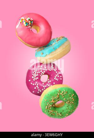 Yummy donuts covered with icing falling on pink background Stock Photo