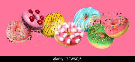 Sweet donuts, chocolate crumbs and sprinkles falling on pink background Stock Photo