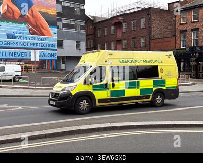 A North West Ambulance Service vehicle driving on Dale Street in Liverpool, UK, past a mural and historic brick architecture. Stock Photo