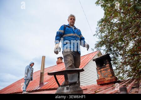 Chimney sweep working on house roof. Professional man repairing building ventilation system. Maintenance service for heater and fireplace. Constructio Stock Photo