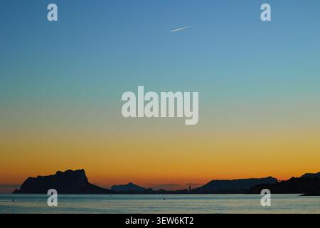 Orange and blue gradient of sunset sky over the sea and rocks in a calm Mediterranean bay Stock Photo