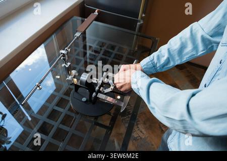 Man sharpening kitchen knife on professional manual machine. Metal blade maintenance device on glass table. Precision tool for grinding and honing met Stock Photo