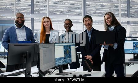 Portrait of smiling multiethnic engineering team optimizing PCB production in factory office. Cheerful colleagues using devices, collaborating to improve microchip processing efficiency, camera A Stock Photo