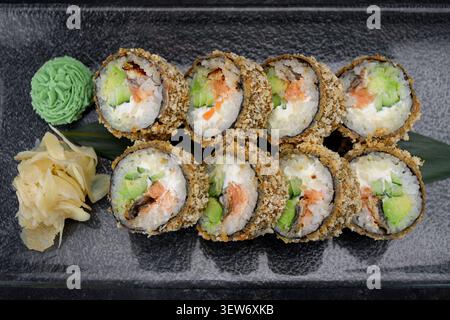 Crispy panko-baked sushi rolls with salmon, avocado, cream cheese, wasabi and pickled ginger on dark glass plate. Japanese fusion restaurant menu. Stock Photo