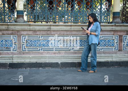 Woman using smartphone by kiosco morisco wall Stock Photo