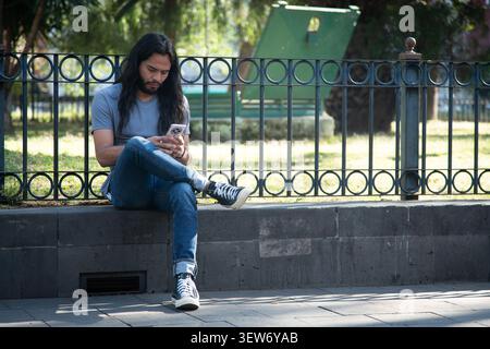 Young man using smartphone sitting on park ledge Stock Photo