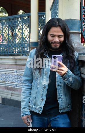Young man smiling using smartphone outdoor with long hair Stock Photo