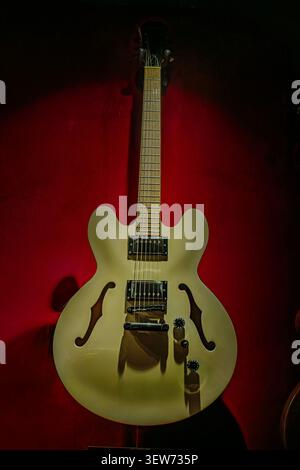 Creamy semi-hollow body electric guitar, featuring light brown neck, standard fretboard, dark headstock with tuning pegs, central single pickup, thin Stock Photo