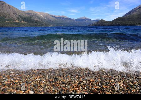 View across a pristine Patagonian lake where gentle waves reach a pebbled shore. Mountain ridges and soft clouds create depth and harmony in the natur Stock Photo