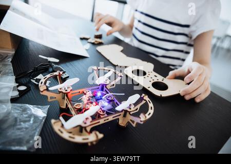 A smart girl puts together a wooden drone with remote control at her home. She explores robotics and learns about STEM. Tools and parts are on the tab Stock Photo
