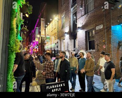 Pedestrians walking past Flanagan's Apple pub on Mathew Street at night in Liverpool, Merseyside, England, illuminated by street lights and signs. Stock Photo