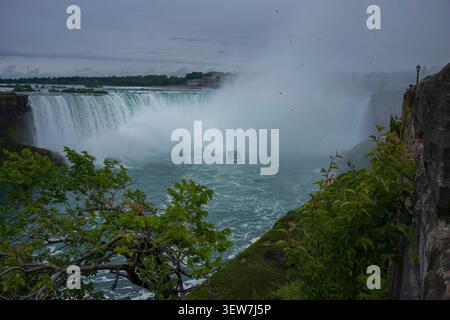 Niagara Falls, Canada - June 22, 2026: Tourist explore on a boat the famous Niagara Falls, seen from Niagara Falls State Park during an overcast day, Stock Photo