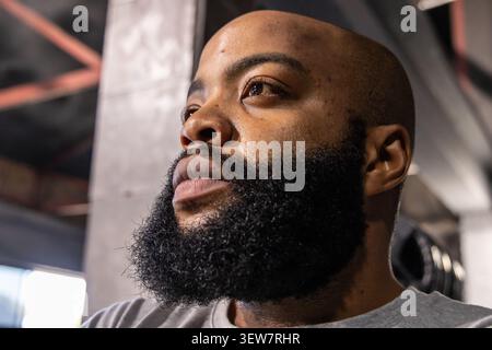 African American man looking upward wearing gray tee in gym near concrete column and weight plates Stock Photo