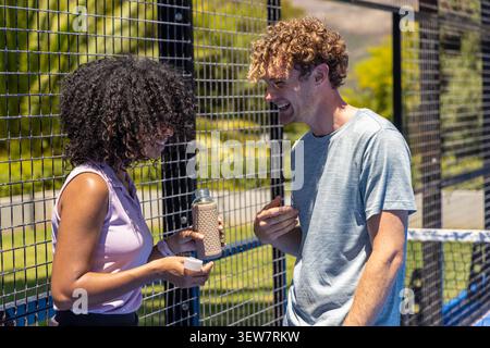 Diverse couple talking while woman holding textured reusable water bottle and cap at sports court Stock Photo
