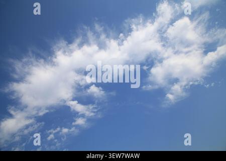 A bright, vivid blue sky filled with soft, wispy white cumulus clouds, creating a calm and uplifting natural scene. Stock Photo